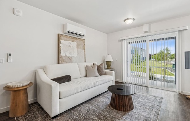 A white couch with a brown pillow is in the middle of a room with a window.