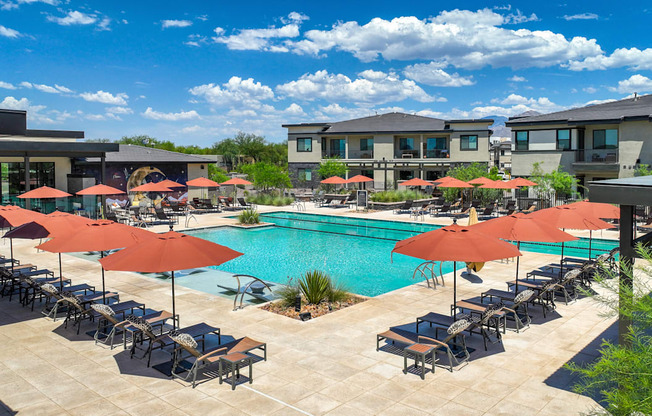 A pool surrounded by chairs and umbrellas with apartment buildings in the background.