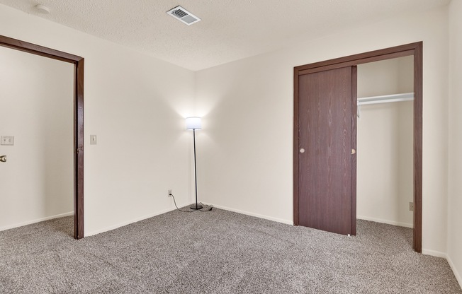 A room with a carpeted floor, a light on a stand, and a brown door.