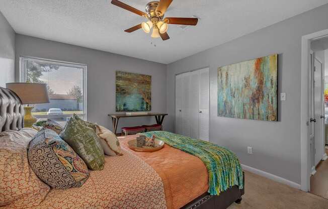 A bedroom with a bed, a ceiling fan, and a painting on the wall.