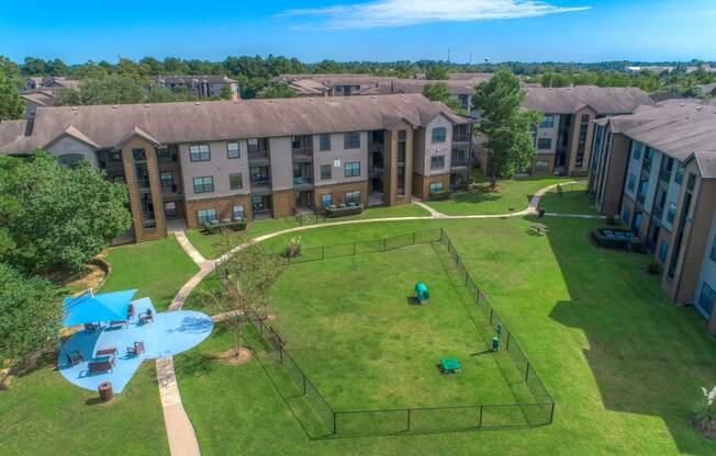 Dog-Friendly Apartments in Spring, TX - Overhead View of Fenced off Dog Park with Seperate Covered Seating Area Surrounded by Lush Greenery.