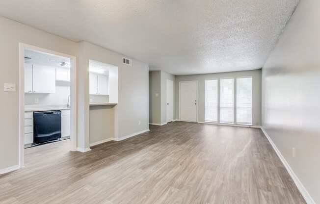 an empty living room and kitchen with a hard wood floor