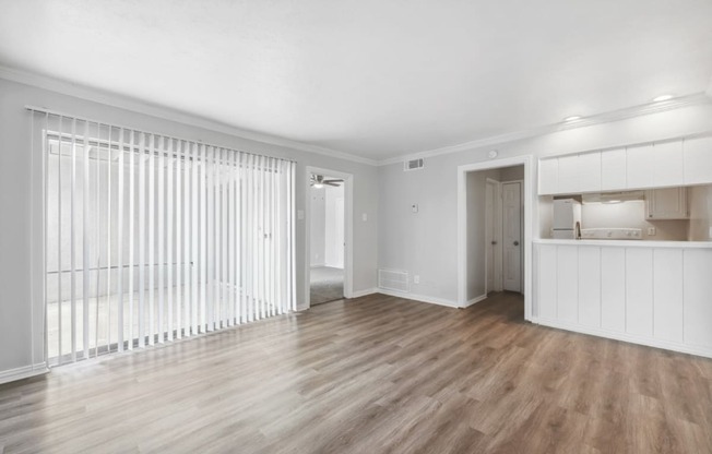 the living room and kitchen of an apartment with white walls and wood floors