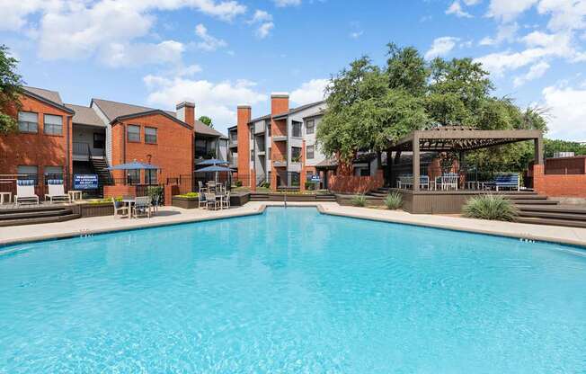 Sparkling swimming pool with pergola lounge area and surrounding brick apartment buildings.