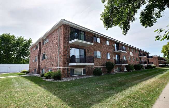 a red brick apartment building with a green lawn and a sidewalk. Fargo, ND Betty Ann Apartments