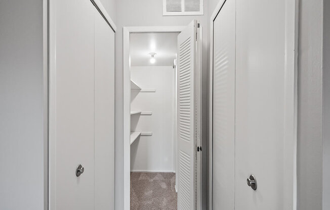 a closet in a small apartment with white doors and a white door to a bathroom