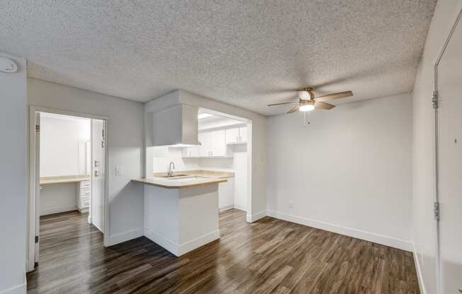 an empty living room with a kitchen and a ceiling fan