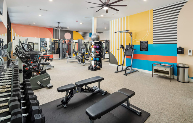 a gym with weights and cardio equipment and a colorful wall