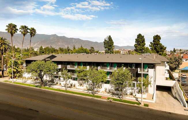 A building with a green roof and white walls is surrounded by trees and palm trees.