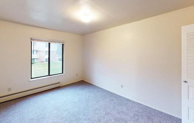 A large bedroom with a window and a carpeted floor at Glen Oaks Apartments, Michigan, 49442