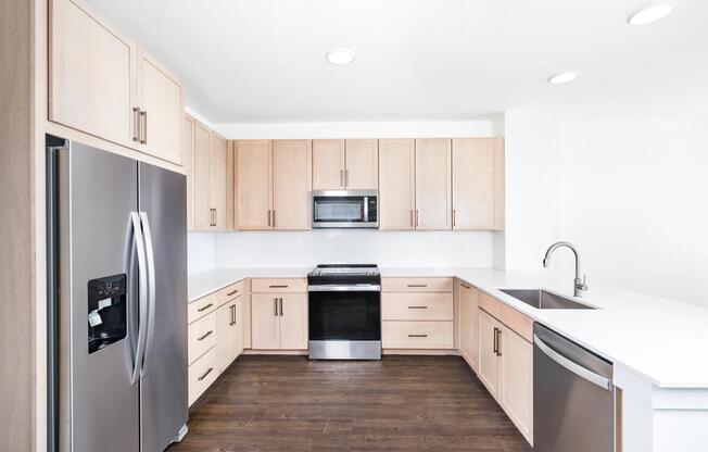 U-shaped kitchen with light wood cabinetry, quartz countertops, and stainless steel appliances arranged for efficient cooking and everyday use.