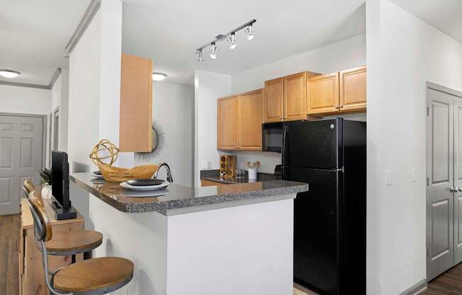 A kitchen with a black refrigerator and wooden cabinets.