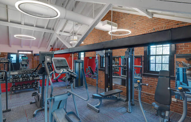 a gym with weights and cardio equipment and a brick wall