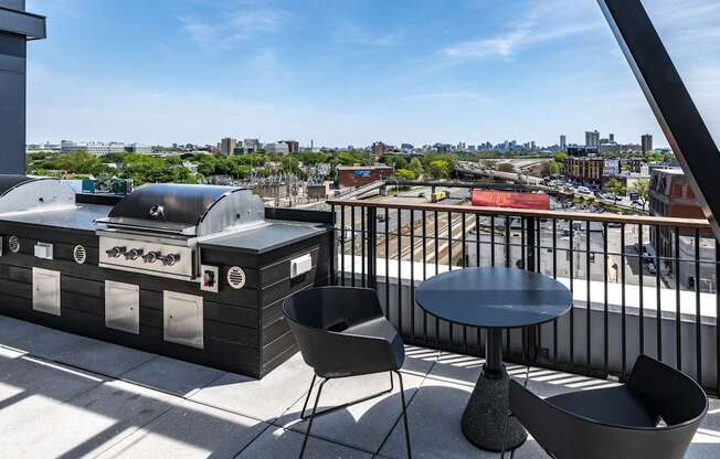 A barbecue grill is on a balcony with a table and chairs.