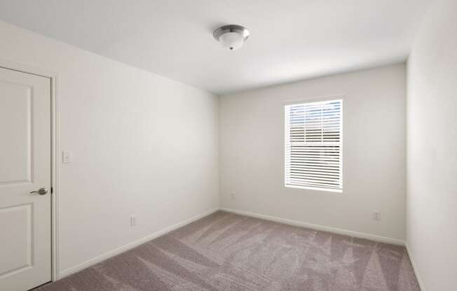 a bedroom with a window, white walls and carpet