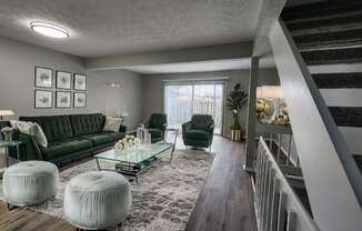 A living room with a green couch, a glass coffee table, and a staircase.