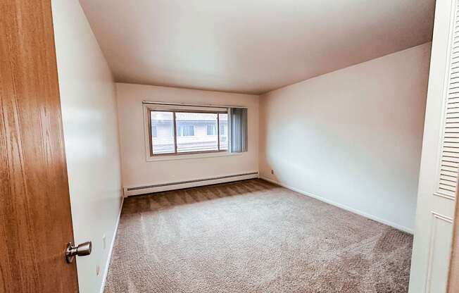 A room with a carpeted floor and a window with blinds.