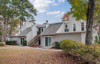 A house with a grey roof and a green door is surrounded by trees.