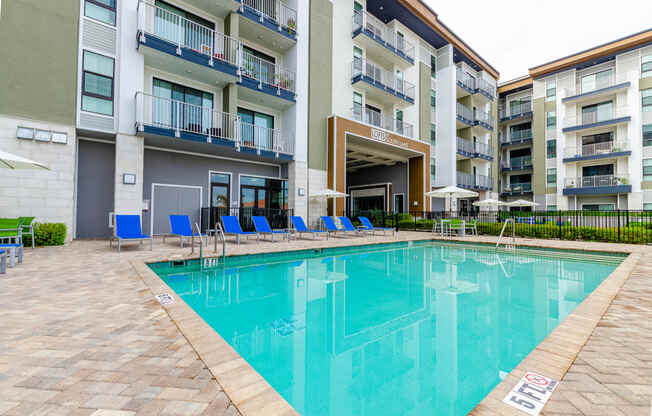 a swimming pool with blue chairs in front of an apartment building