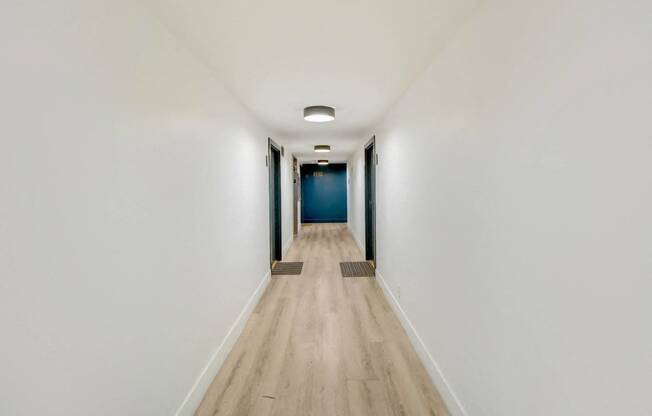 a long hallway with white walls and wood floors and a blue door at the end