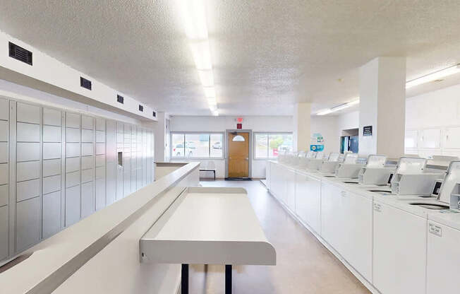 A long white table is in the middle of a room with white cabinets on the walls.