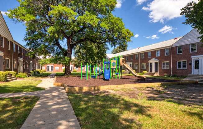 A playground with a slide and a tree in front of a building.