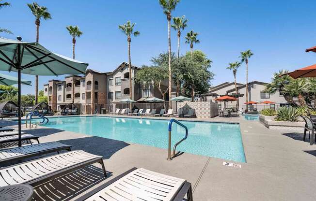 A pool surrounded by palm trees and sun loungers. at Lazo Apartment Homes, Chandler Arizona