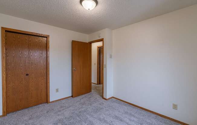 a bedroom with carpet and a door to a hallway. Fargo, ND Crescent Park Apartments