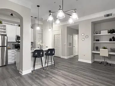 A kitchen with a refrigerator, bar stools, and a dining table.