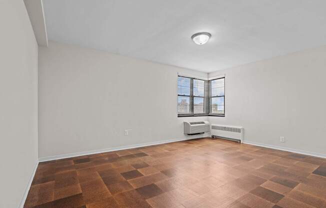 A room with a brown floor and a window with blinds.