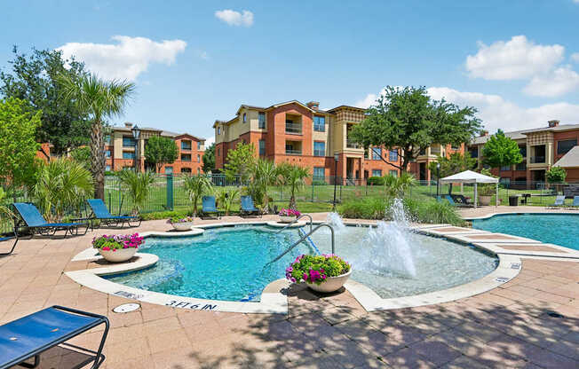 A pool with a fountain in the middle of a patio with chairs around it.