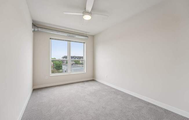 A room with a ceiling fan and a window overlooking a street.
