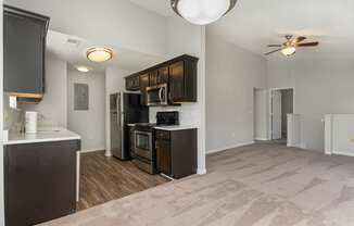 an empty living room with a kitchen and a ceiling fan