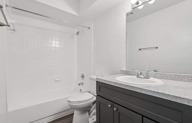 A white toilet sits in a bathroom with a white tub and a sink.