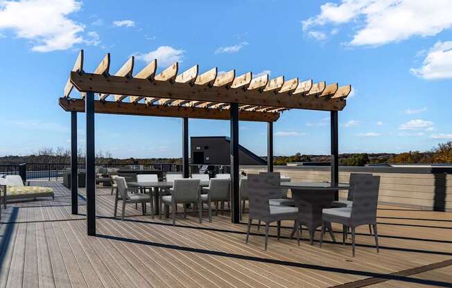 A wooden deck with tables and chairs under a pergola.