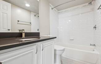 A white toilet sits in a bathroom with a white tub and sink.