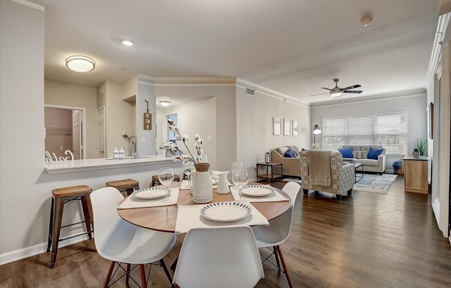 a dining area with a table and chairs and a living room in the background